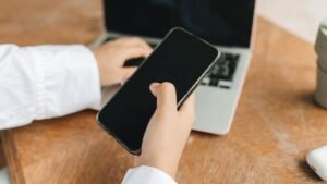 Person using smartphone and laptop in a home office setup, ideal for remote work concepts.