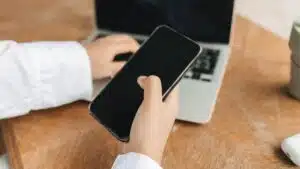 Person using smartphone and laptop in a home office setup, ideal for remote work concepts.