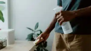 A man using a multi-purpose cleaner and sponge to clean a table indoors, emphasizing hygiene.