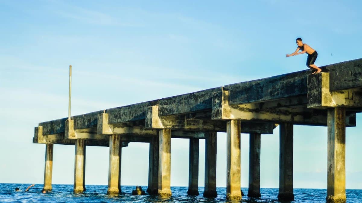 A man stands ready to jump off an ocean pier, capturing an adventurous moment.