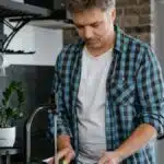 A man washing dishes at a sink in a contemporary kitchen setting.