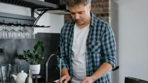 A man washing dishes at a sink in a contemporary kitchen setting.