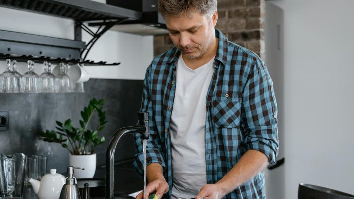 A man washing dishes at a sink in a contemporary kitchen setting.