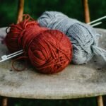 Two yarn balls with knitting needles on an old chair outdoors. Perfect for crafting enthusiasts.