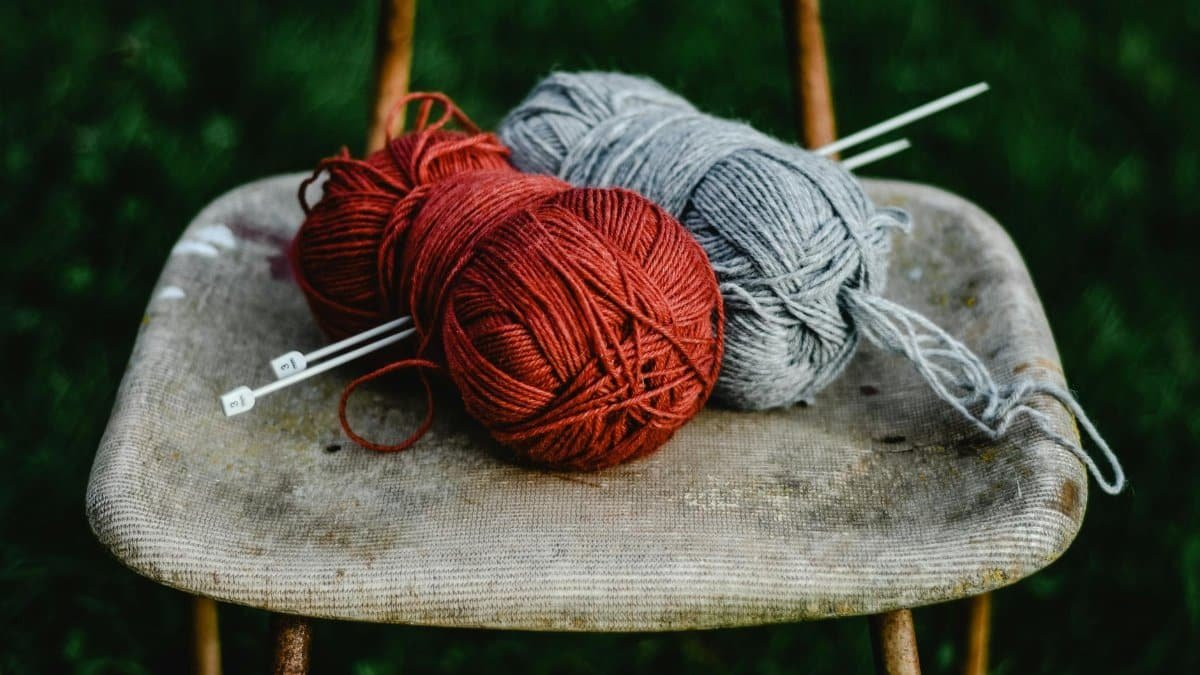 Two yarn balls with knitting needles on an old chair outdoors. Perfect for crafting enthusiasts.
