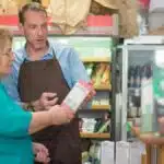 A shopkeeper assists a senior customer in a local Portuguese grocery store.
