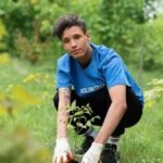 A dedicated volunteer planting a tree sapling in a lush green park environment.