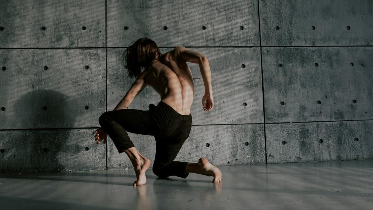 A male dancer performs a dynamic pose against a textured wall, showcasing flexibility and artistic expression.