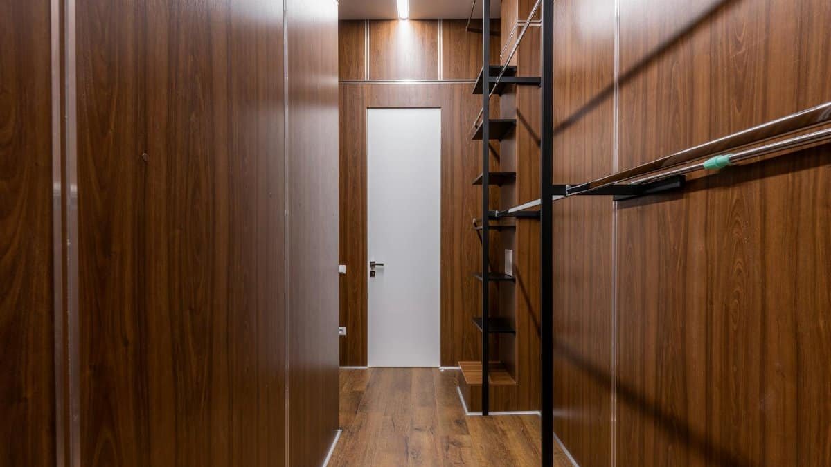 Empty black shelves and racks placed near brown walls in corridor with minimalist style with white door and glowing illumination