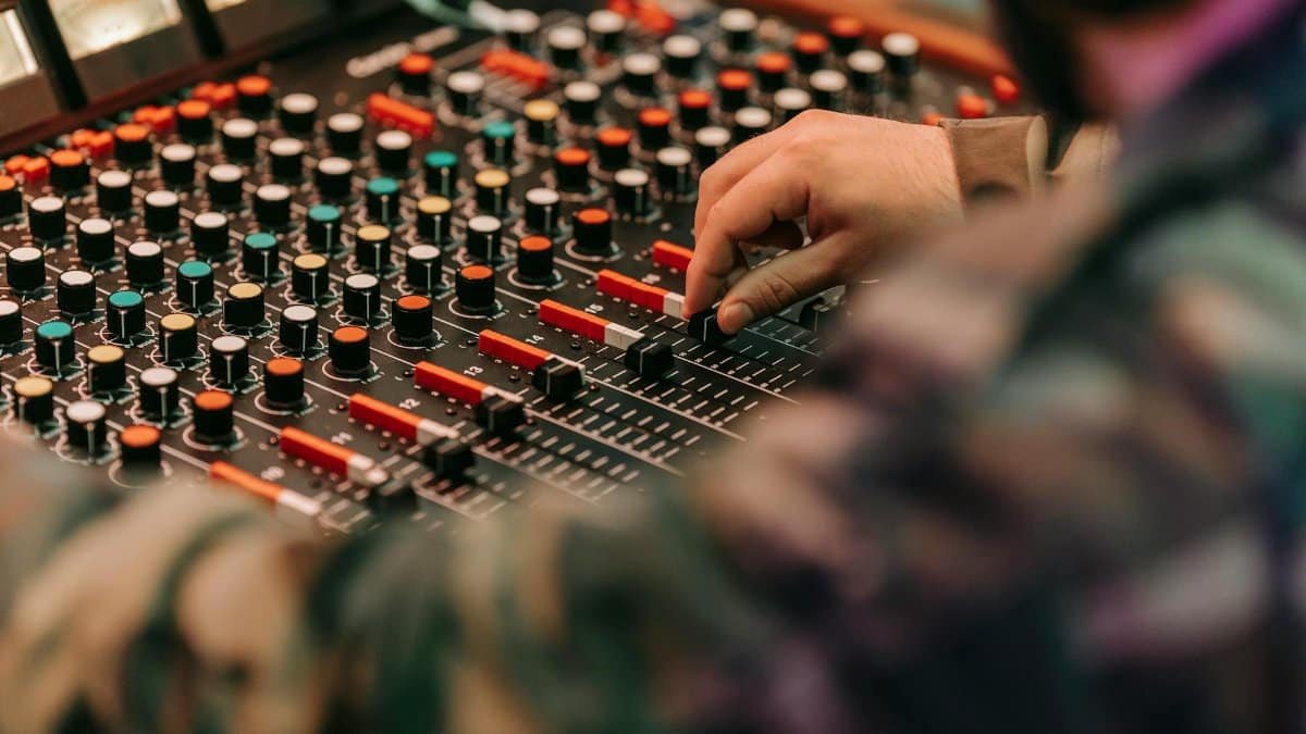 Hand adjusting controls on an audio mixer in a recording studio setting.