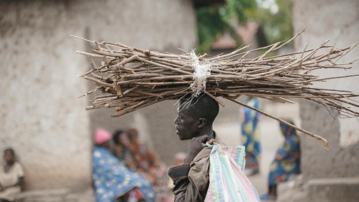 Profile of African man carrying firewood on head, depicting traditional village life.