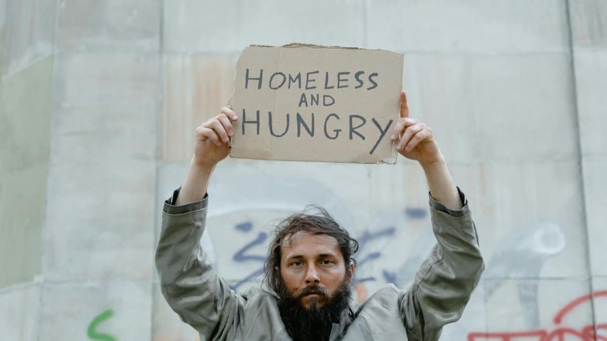 A homeless man holds a cardboard sign reading 'Homeless and Hungry.'