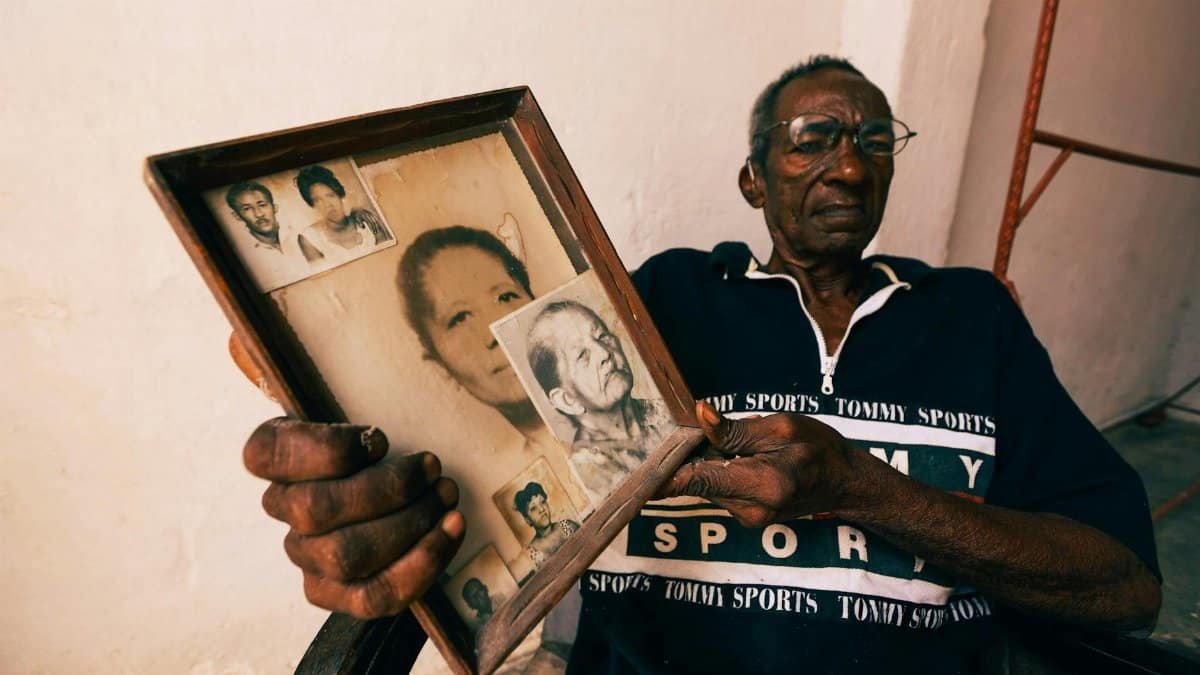 Senior man reflects on legacy with framed family photos, creating a nostalgic atmosphere.