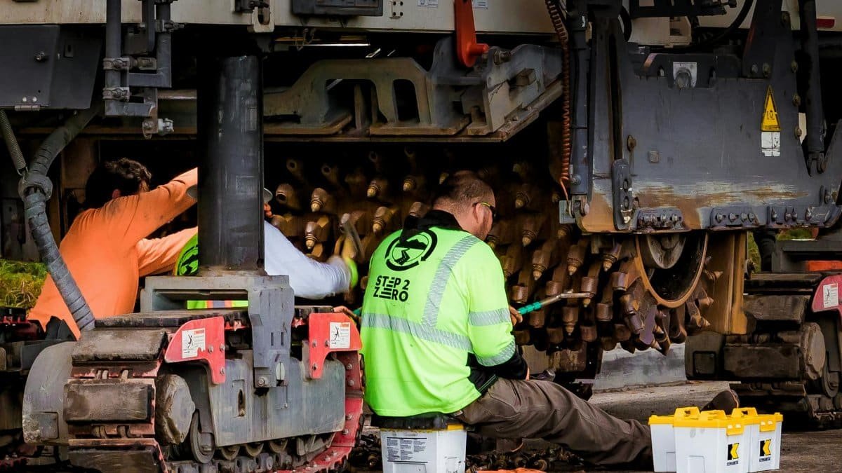 Engineers performing maintenance on construction equipment in an industrial workshop setting.