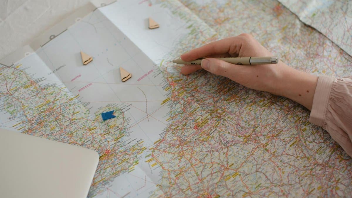 Hand holding pen over Europe map, planning travel route with markers.