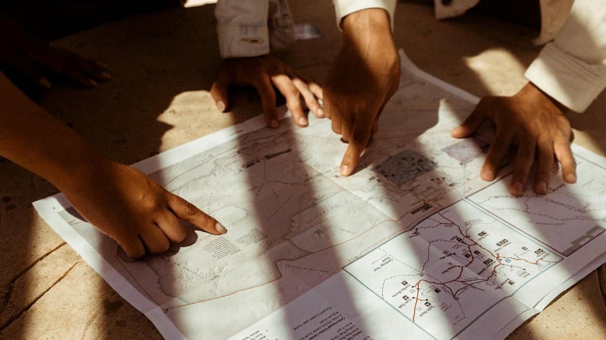 Group of hands pointing at a detailed map, planning an adventure trip in sunlight.