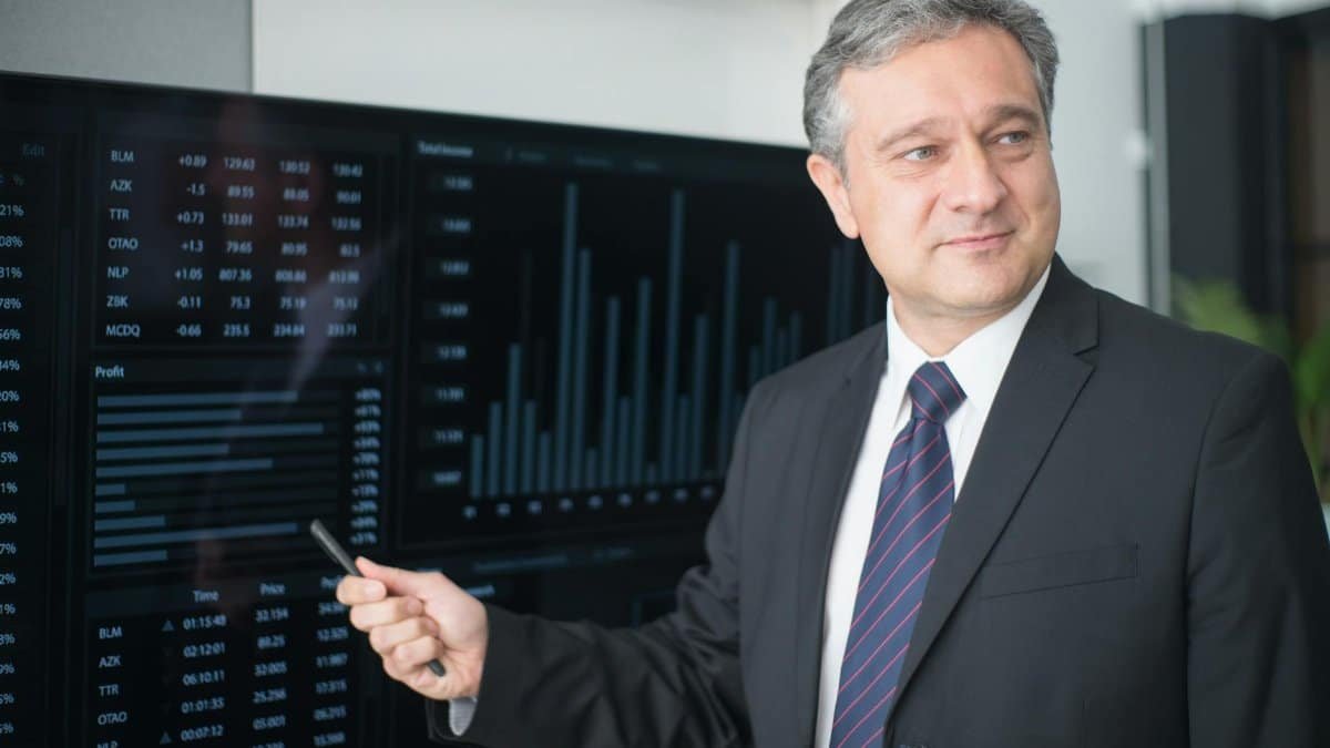 Professional man in suit reviewing financial charts on monitor, showcasing stock market trends.