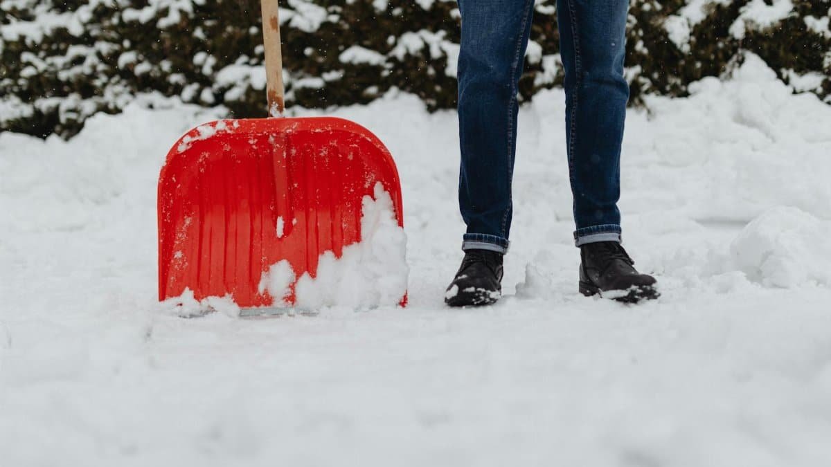 A person shoveling heavy winter snowfall using a red snow shovel. Outdoor winter scene.