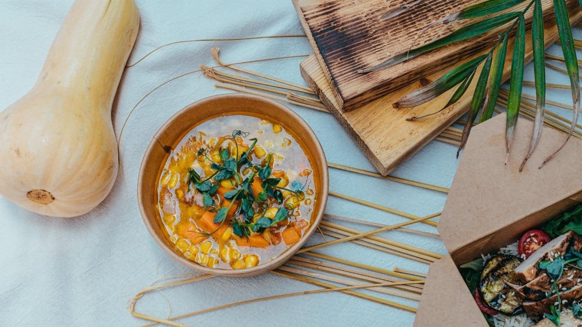 A cozy flat lay of a rustic table setting featuring a bowl of pumpkin soup and grilled food.
