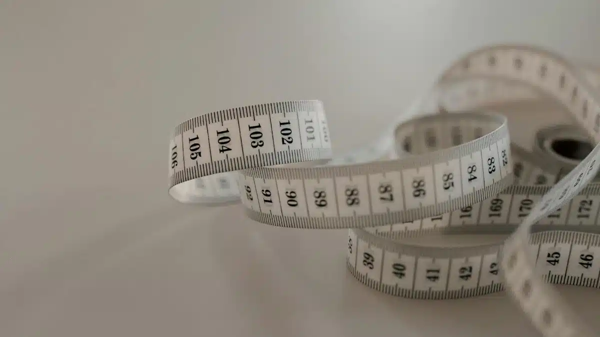 White tape measure with black numbers, coiled loosely on a plain surface.