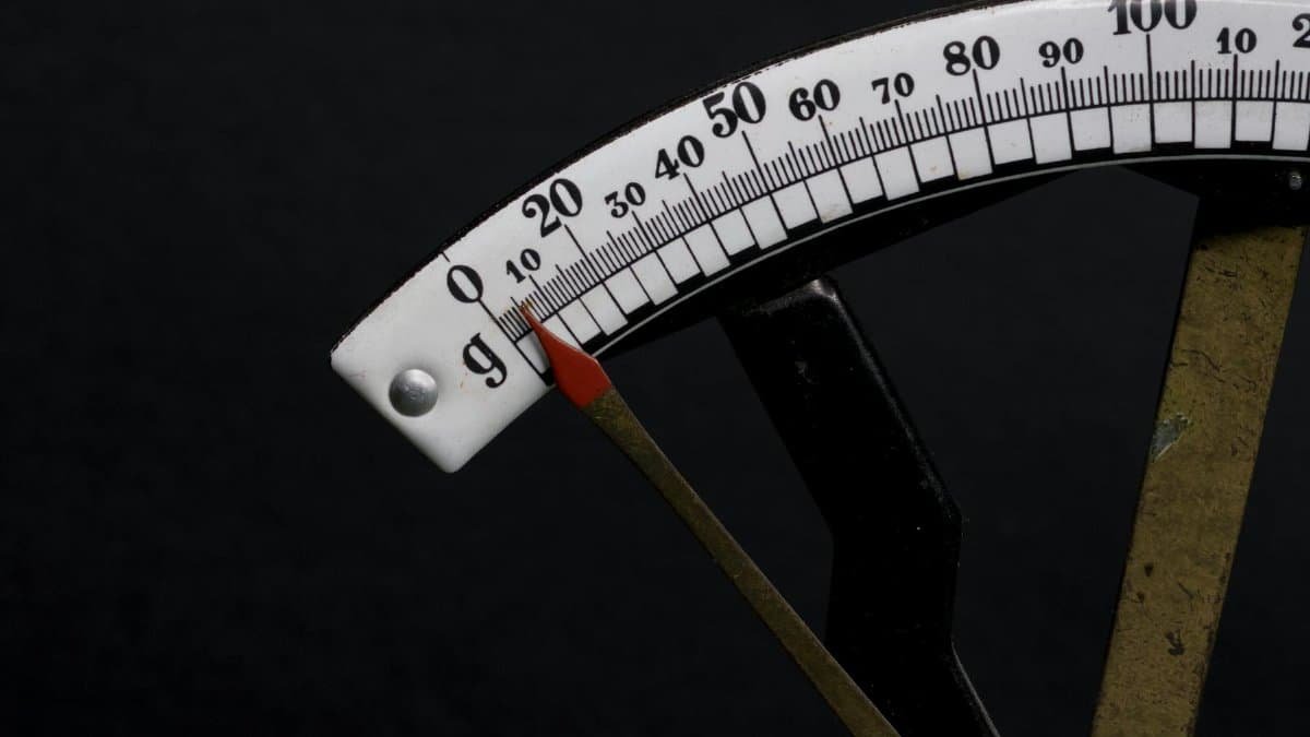 Detailed close-up image of a vintage analog weighing scale with a pointer against a black background.