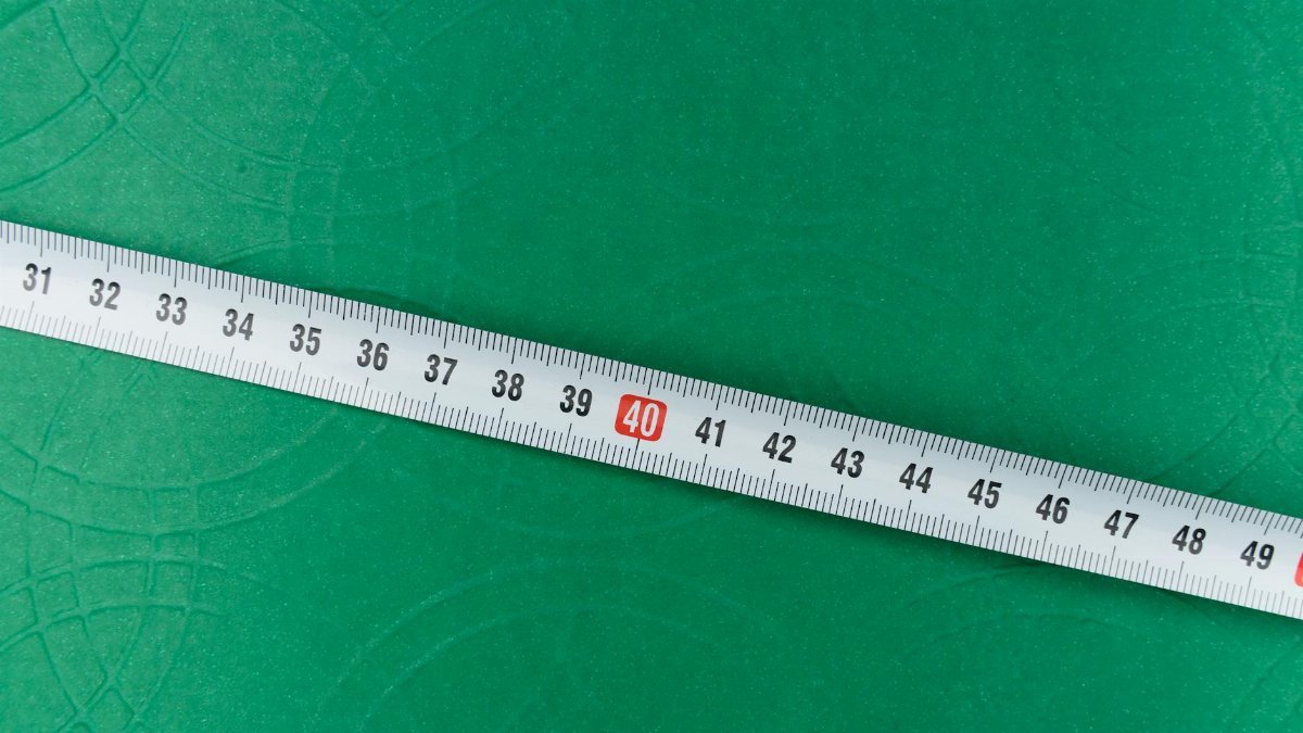 A measuring tape lying diagonally on a green textured surface.