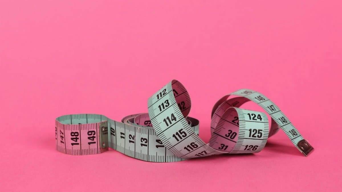 Close-up of a measuring tape on a vibrant pink background for design use.