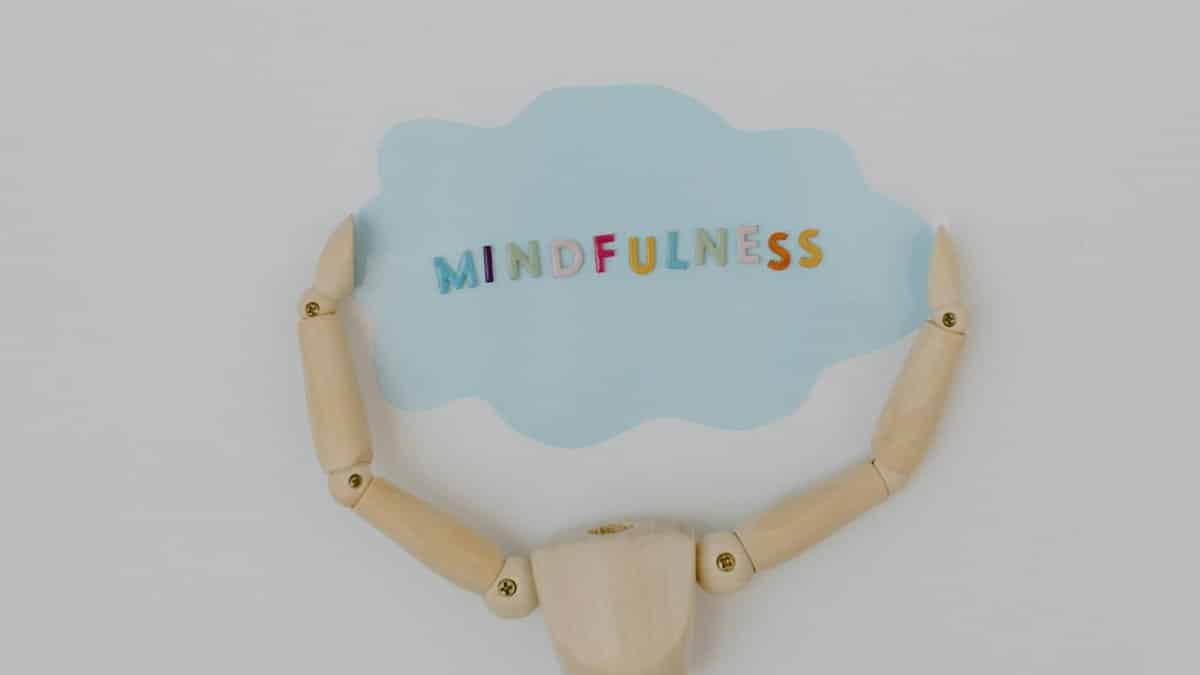 Wooden mannequin arms holding a blue cloud with 'Mindfulness' text, promoting self-awareness.