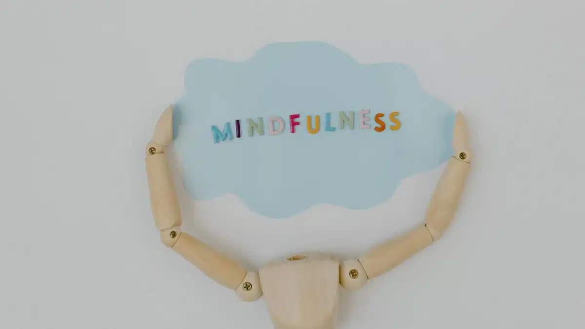 Wooden mannequin arms holding a blue cloud with 'Mindfulness' text, promoting self-awareness.