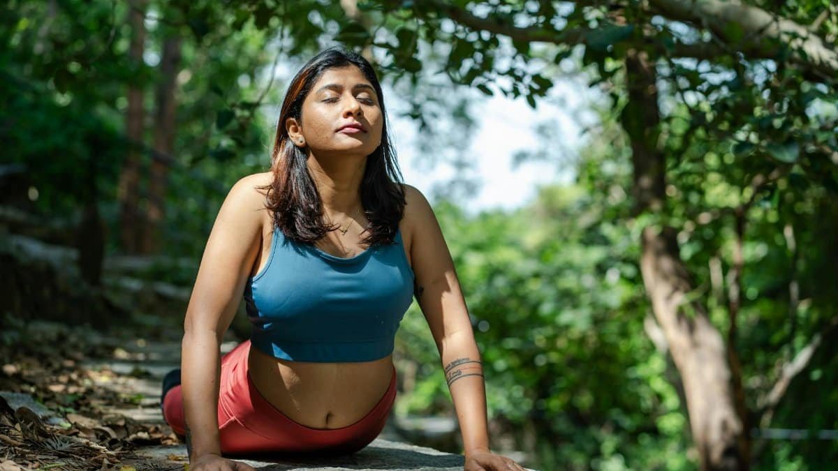 Woman doing yoga outdoors in a lush green forest, enjoying nature.