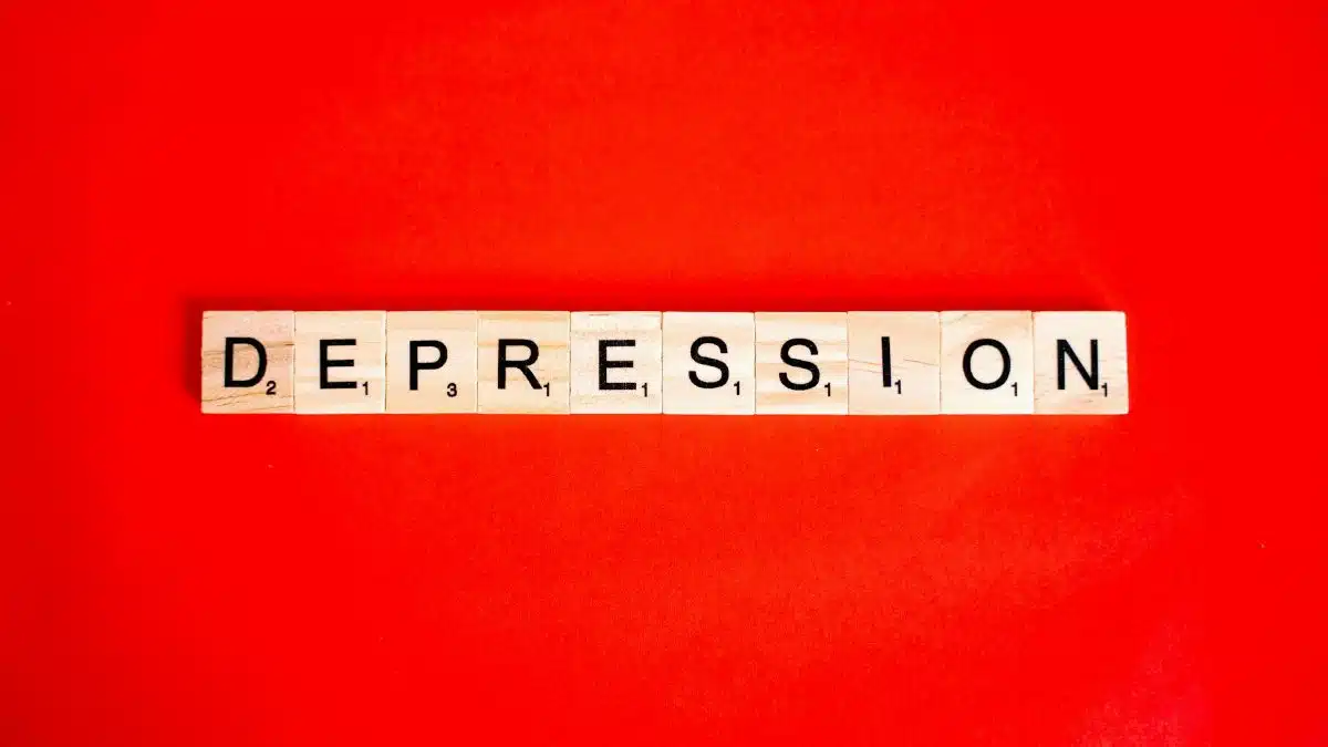 Word depression spelled with letter tiles on vibrant red background, highlighting mental health theme.