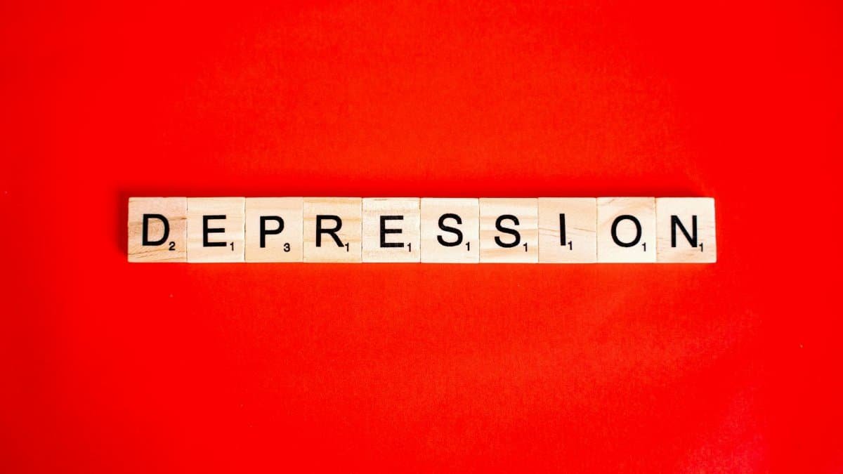 Word depression spelled with letter tiles on vibrant red background, highlighting mental health theme.