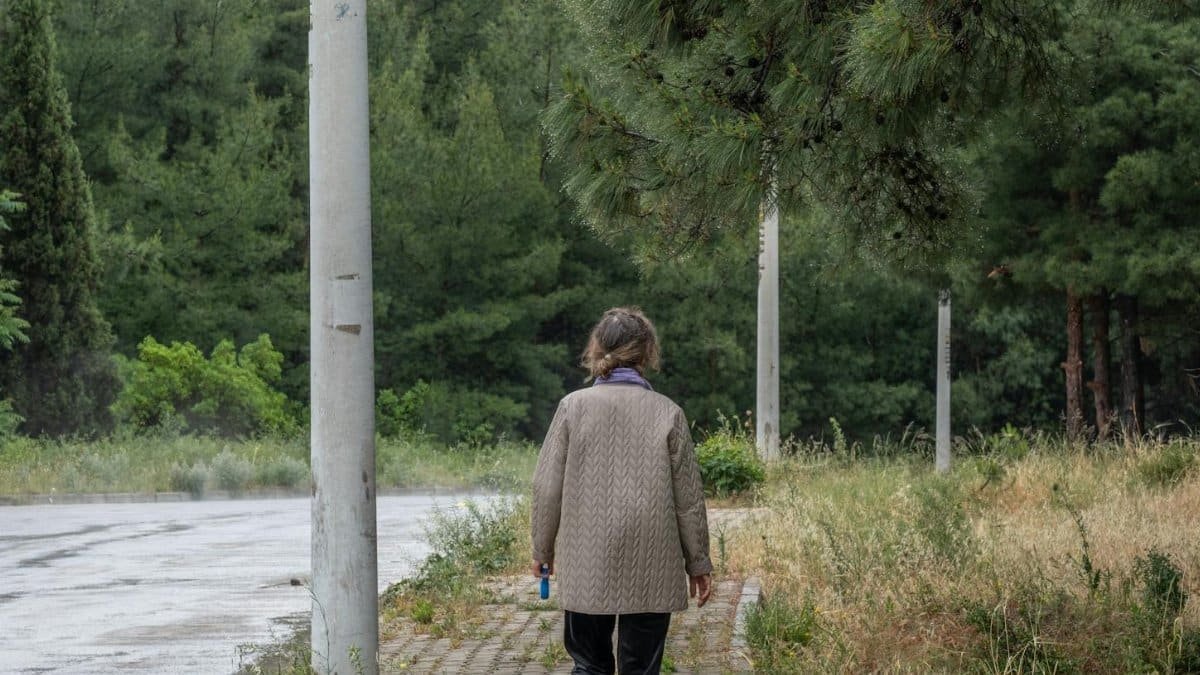 Woman walking small dog on a quiet forest path, surrounded by greenery.