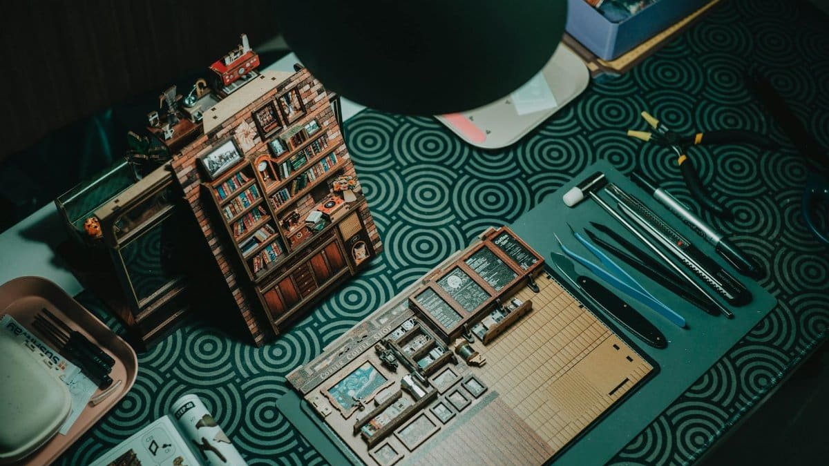 A detailed miniature bookshelf crafting setup with tools on a patterned table.