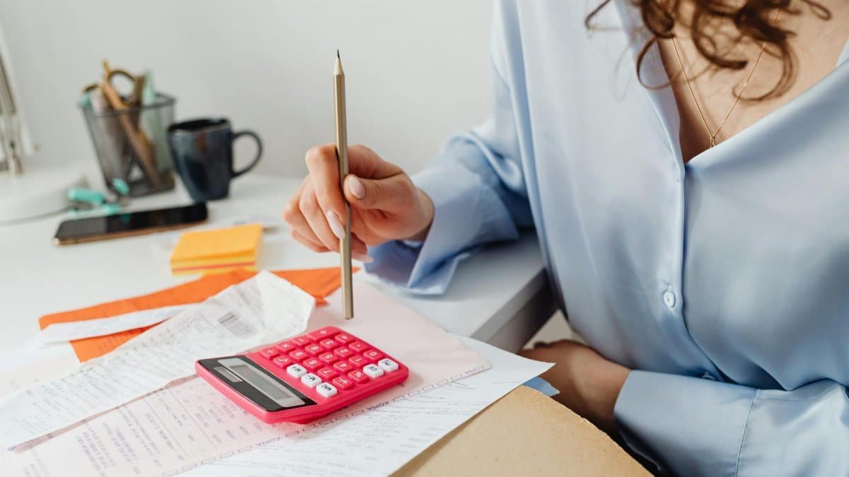 A woman is calculating expenses using a calculator and papers at her desk.