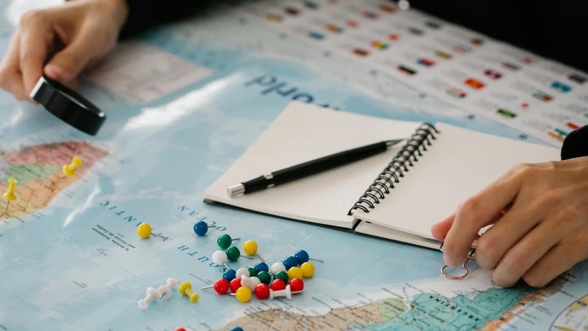 Close-up of hands planning a trip with map, pins, and notebook.