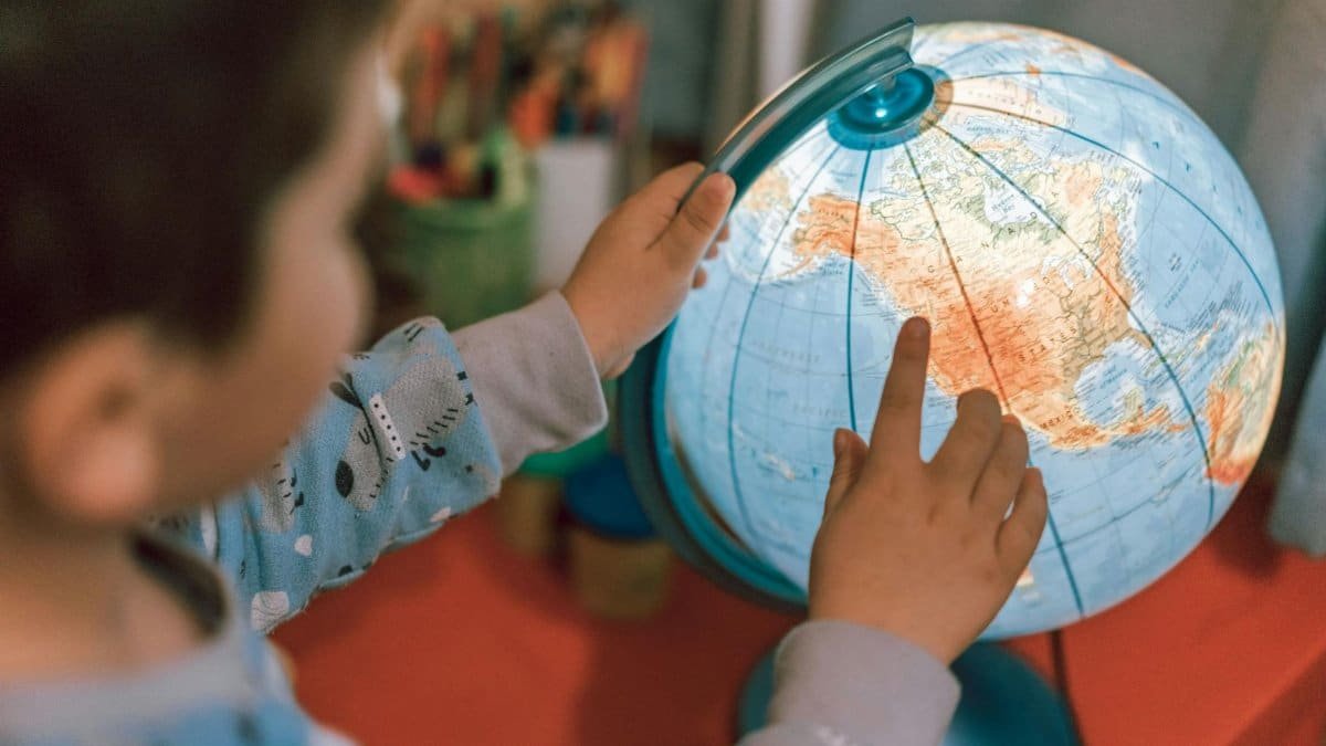 A child discovers geography by pointing at a globe, fostering curiosity and learning.