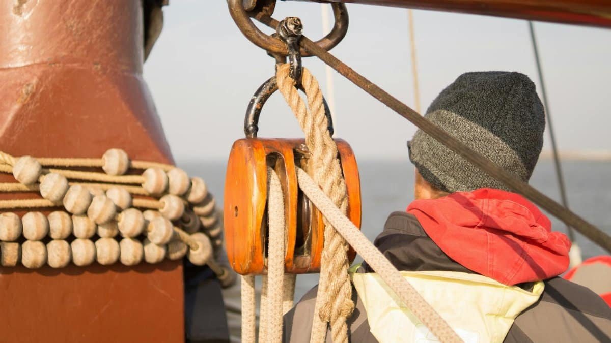 Sailor adjusting rope and pulley system onboard a sailing vessel, navigating the open sea.