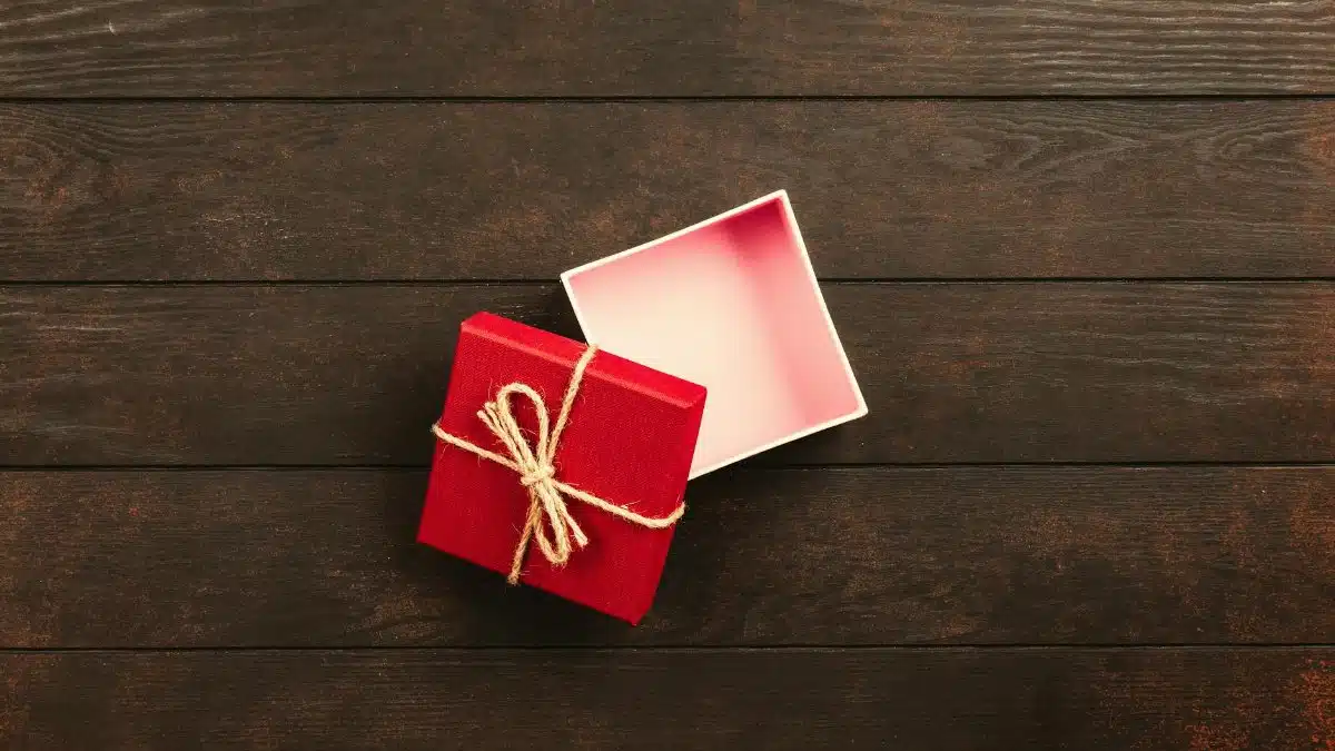 Top view of an open red gift box tied with twine on a wooden surface.