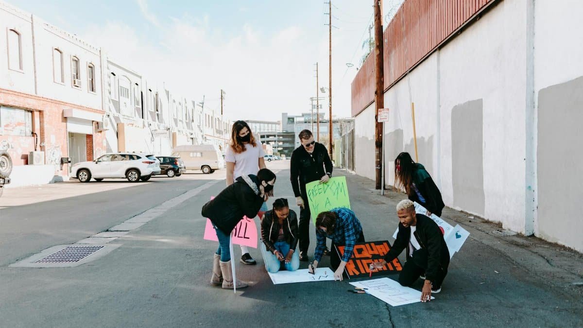 Diverse group of people preparing signs for a protest in an urban setting.