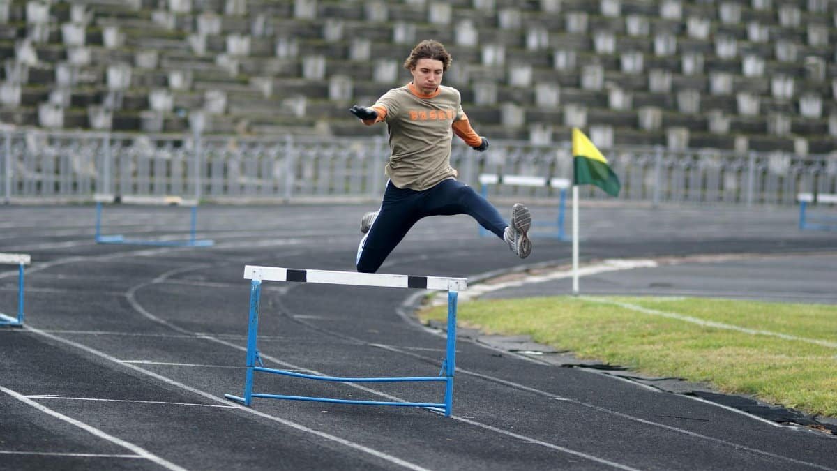 Athlete demonstrating speed and agility while jumping hurdles during track event.