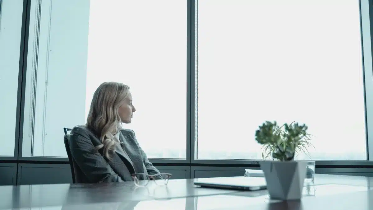 A businesswoman in a suit looking out the window of a contemporary office with a modern setup.