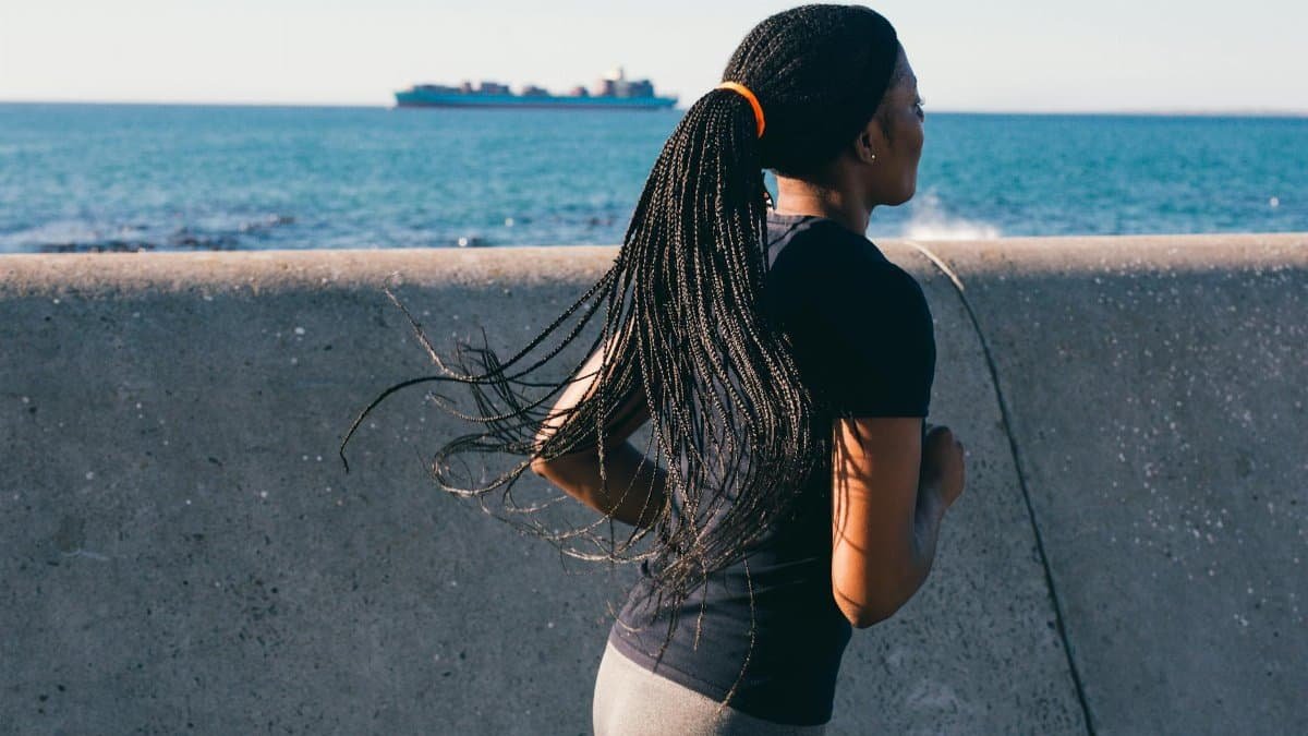 Black woman running along a sea wall, promoting fitness and healthy living.