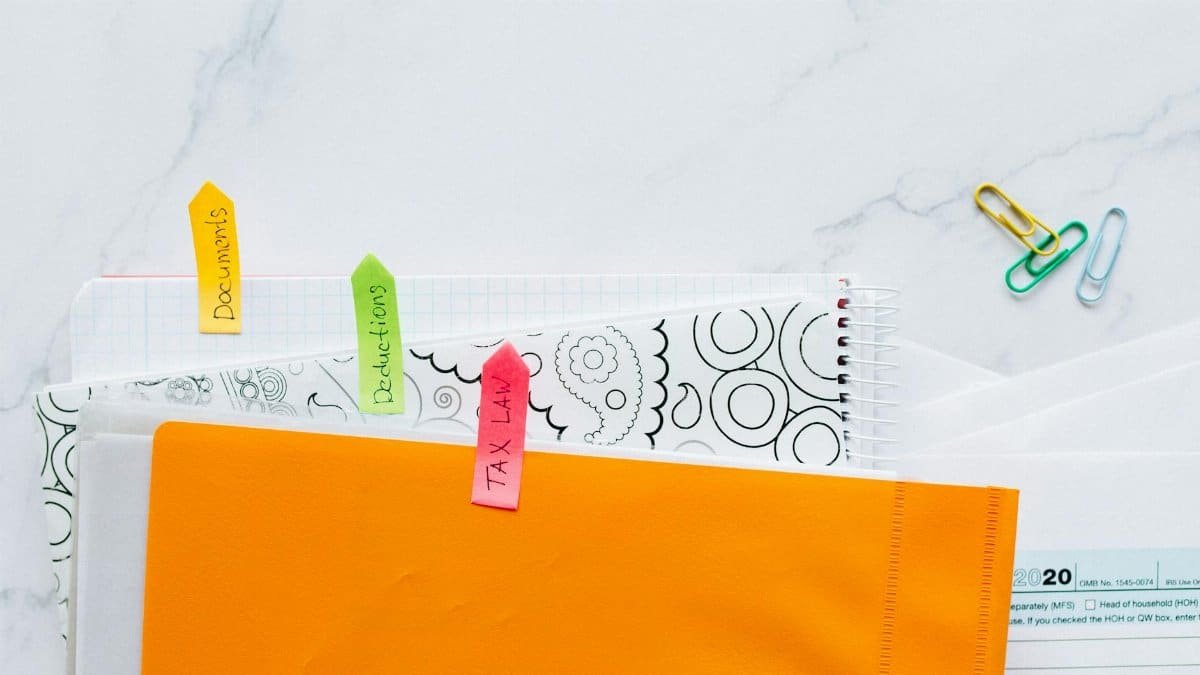 Top view of tax documents organized with colorful sticky notes on a marble desk.
