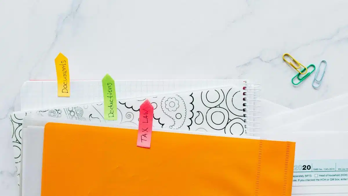 Top view of tax documents organized with colorful sticky notes on a marble desk.