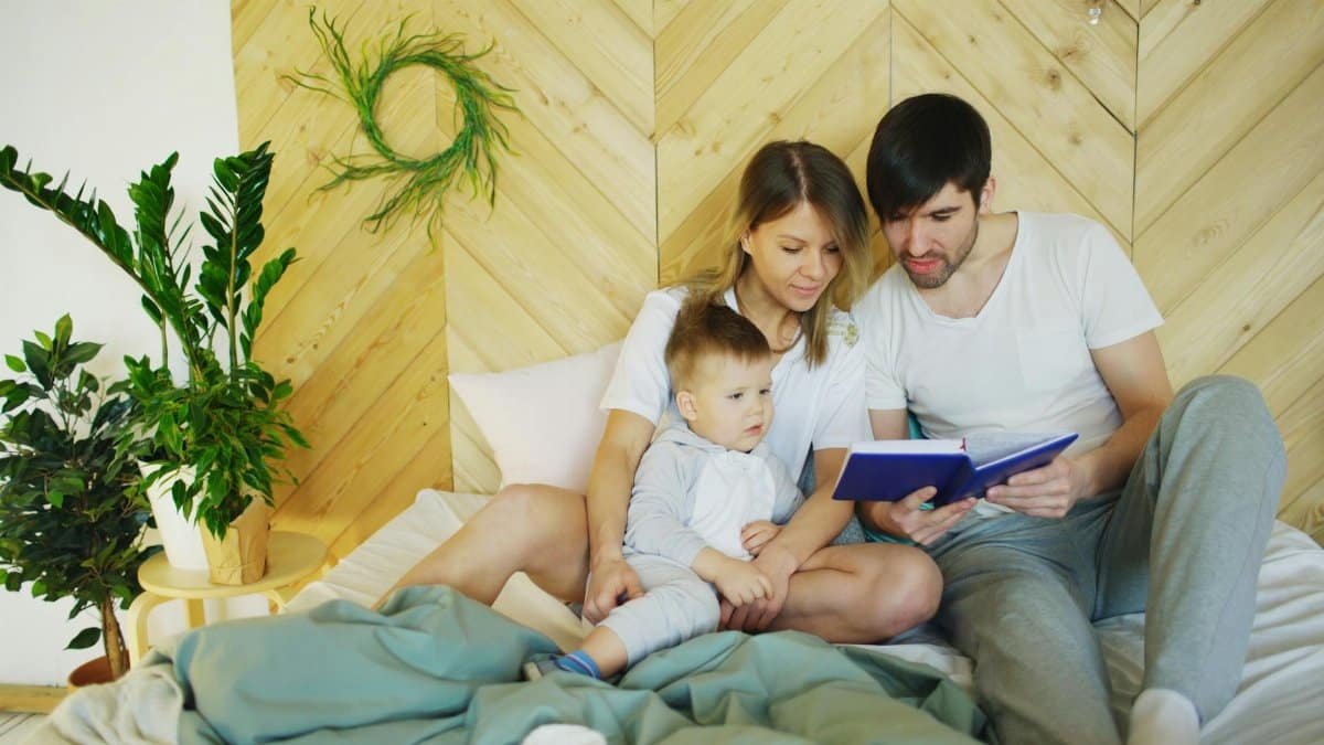 Loving parents reading a book with their child in a cozy bedroom setting, promoting family bonding.