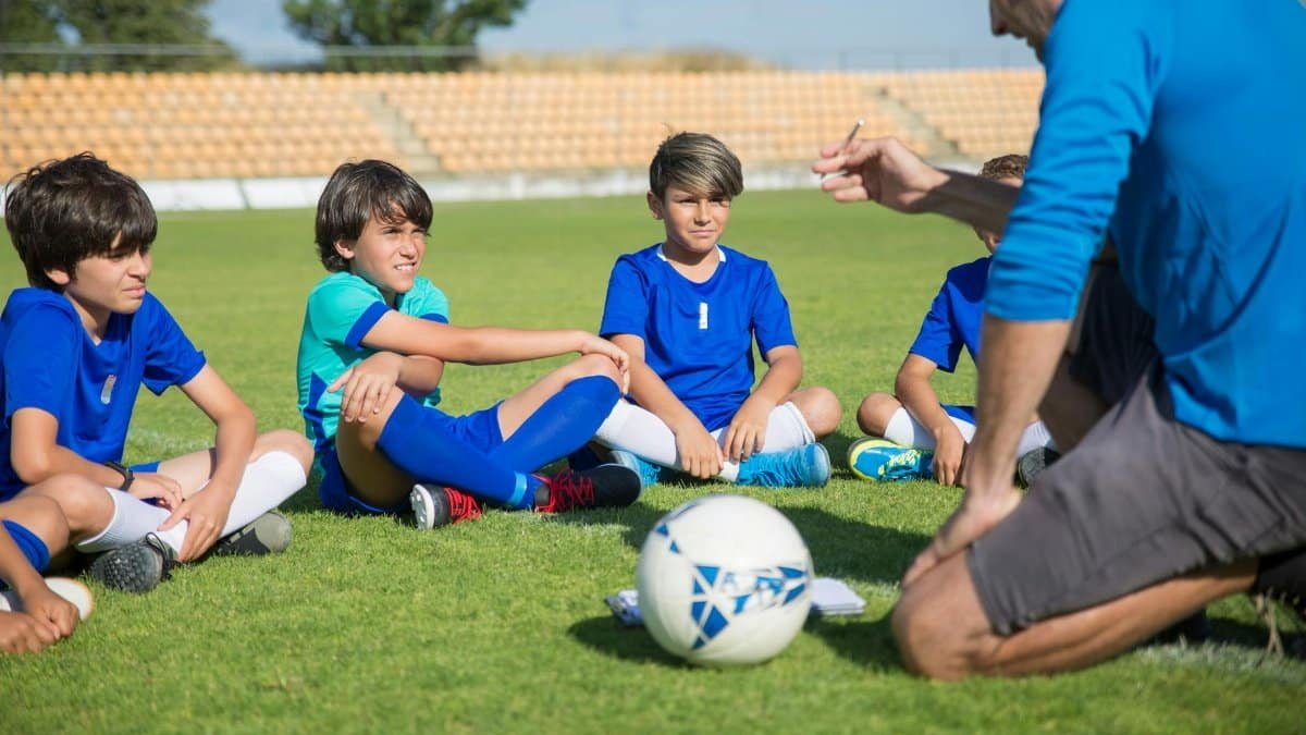 Boys listen intently to their soccer coach on a sunny soccer field.