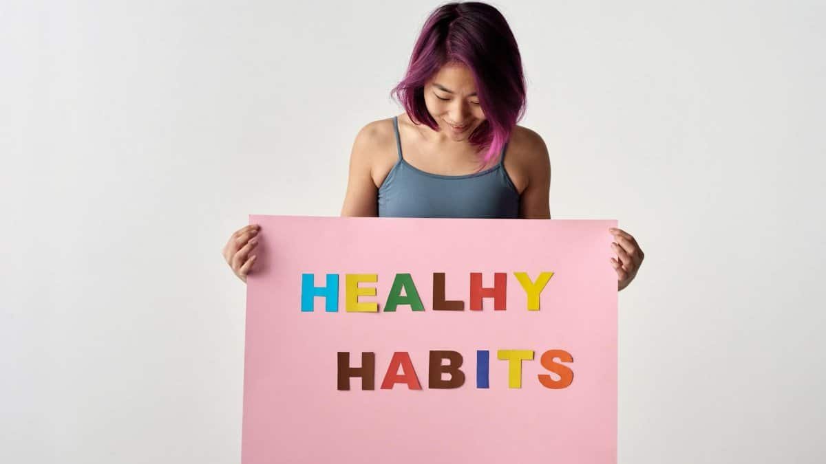 Asian woman holding a colorful 'Healthy Habits' sign in a studio setting, promoting wellness.
