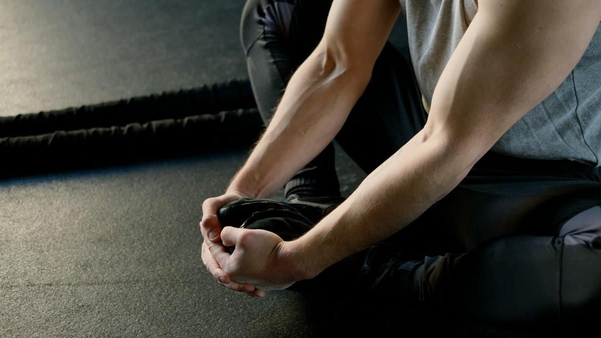 Man sitting on gym floor, stretching legs, preparing for workout routine.