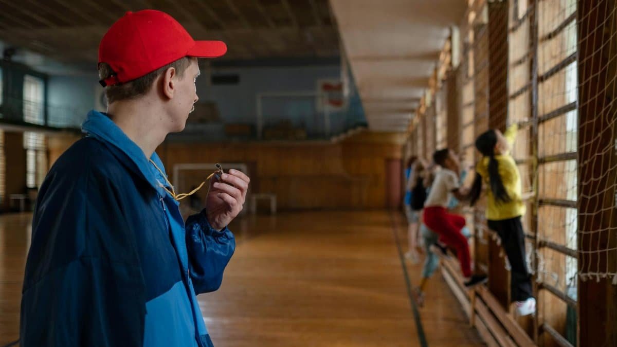 A coach guides young students during a physical education session in an indoor gym.